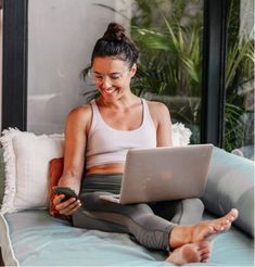 a woman sitting on a bed looking at her cell phone and laptop