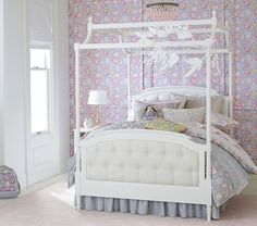 a white bed sitting in a bedroom next to a wall covered in pink and purple flowers