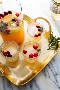 three glasses filled with orange juice and cranberries on a gold serving platter