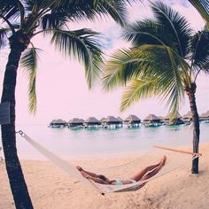 a man laying in a hammock between two palm trees on the beach,