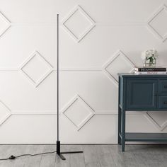 a black floor lamp next to a blue table with a white flower on it and a gray cabinet