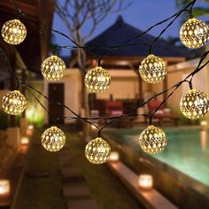 some lights are hanging from a tree in front of a swimming pool at night time