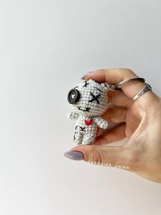 a hand holding a small white crocheted dog keychain with a red heart on it