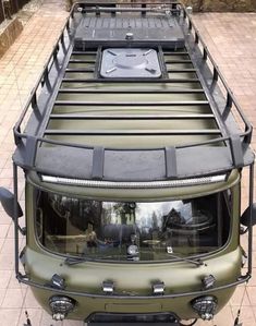 an army green truck parked on the side of a brick road in front of a building