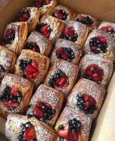 a box filled with lots of pastries covered in powdered sugar and fresh berries