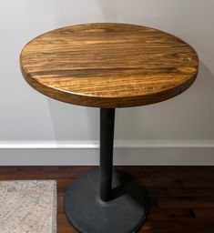 a round wooden table sitting on top of a hard wood floor next to a white wall