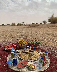 a table topped with lots of food sitting on top of a red rug in the middle of a desert