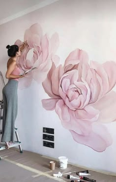 a woman is painting a large flower on the wall