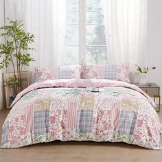 a bed covered in pink and green comforter next to a window with white curtains