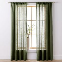 a window with green curtains in front of a white wall and wooden flooring next to a potted plant