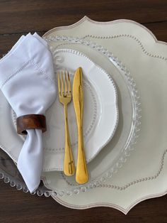 a white plate topped with gold colored utensils next to a wooden fork and knife