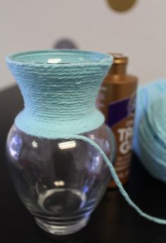 a glass vase sitting on top of a table next to yarn