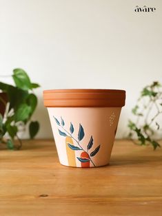 a flower pot sitting on top of a wooden table next to a green leafy plant