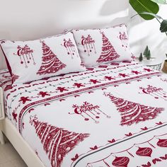 a bed covered in red and white christmas themed bedspreads with trees on them