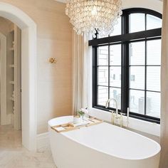 a large white bathtub sitting next to a window in a bathroom under a chandelier