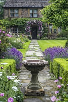 a garden with purple flowers and lavender bushes in front of a stone path leading to a house