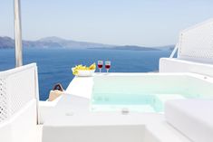 two glasses of wine are sitting on the edge of a balcony with a jacuzzi tub