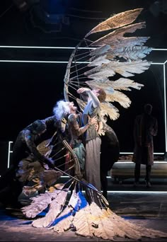 two men and a woman standing in front of a spiral staircase with feathers on it