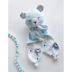 a blue teddy bear laying on top of a white floor next to a beaded necklace