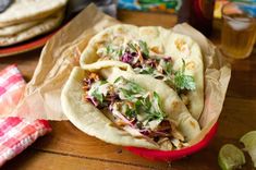 three tacos with shredded cabbage and cilantro on a table next to limes