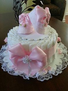 a three tiered cake decorated with pink bows and diapers on a lace doily