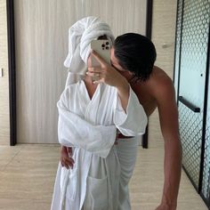 a man taking a selfie in front of a mirror wearing a white robe and holding a cell phone