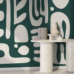 a white table sitting in front of a wall with green and white designs on it