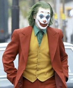 a man in a suit and clown mask walking down the street with his hands on his hips