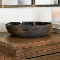 a black bowl sitting on top of a wooden table next to a book and mirror