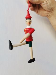 a hand holding a small wooden ornament with a red hat and green pants