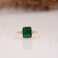 an emerald and diamond ring on a white surface