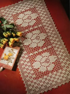 an old doily with roses on it next to a bouquet of flowers and a book