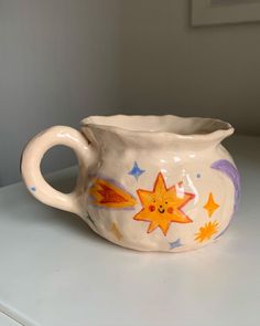 a white vase with stars and planets painted on the side sitting on a counter top