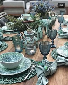 the table is set with dishes, cups and vases in blue green color scheme