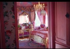 a bedroom with pink walls and floral wallpaper, chandelier and bedding