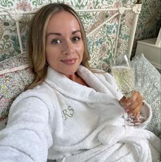 a woman in a bathrobe holding a glass of wine on a bed with floral wallpaper