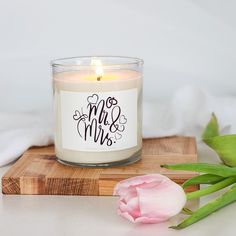 a white candle sitting on top of a wooden cutting board next to a pink tulip