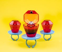 three red and yellow glass vases on blue bases with a diamond ring in the middle