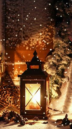 a lit lantern sitting on top of a snow covered ground next to a christmas tree