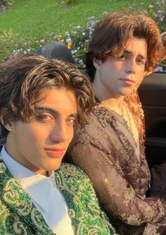 two young men sitting in the back seat of a car, one wearing a green and white jacket