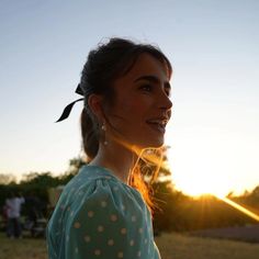 a woman standing in front of the sun with her hair pulled back and wearing a polka dot blouse