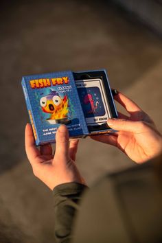 a person holding up a card game in front of their face with the box open