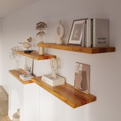 two wooden shelves with books, vases and other items on them against a white wall