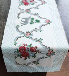 a white table cloth with red flowers and animals on it, sitting on a wooden surface