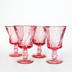 four pink glass goblets sitting side by side on a white surface with no background