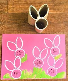 toilet paper roll bunny stamps on a pink background next to a cup with rolled up easter eggs