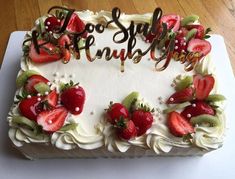 a white cake with strawberries and kiwis on it that says happy birthday