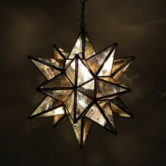 a stained glass star hanging from a chain on a dark background with light shining through it