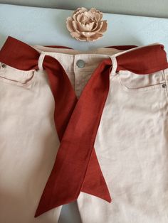 a pair of white jeans with a red ribbon tied around the waist and an orange flower on top