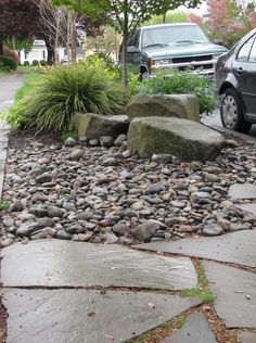 a car is parked in front of some rocks and plants on the side of the road